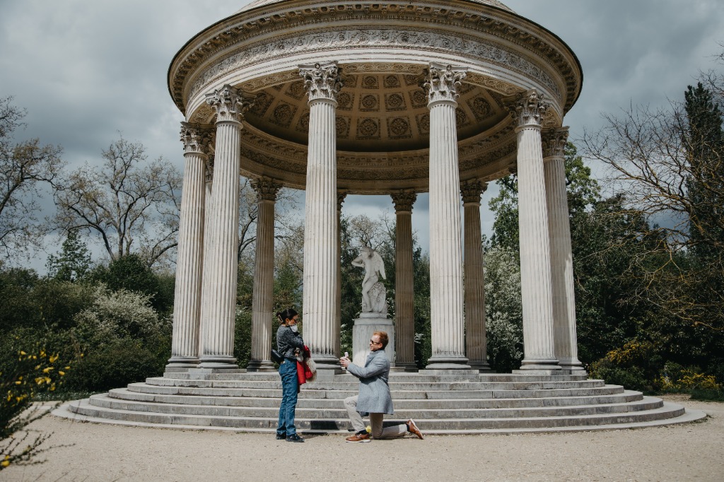 Glendon proposing to Amanda at the Temple of Love in Versailles with Cupid statue behind them